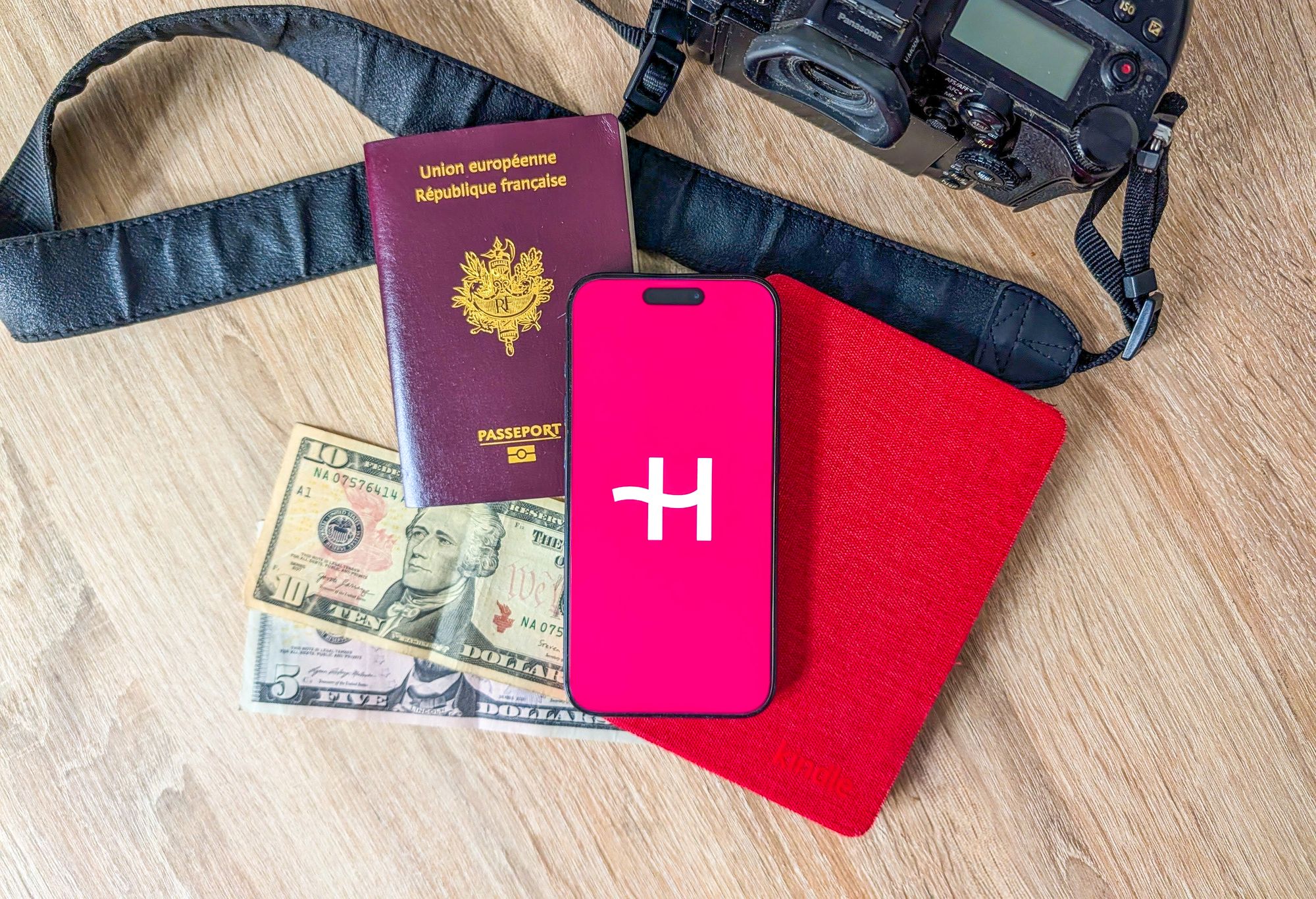 Appareil photo, passeport, kindle et quelques dollars sur une table, avec un téléphone allumé sur l'application Holafly