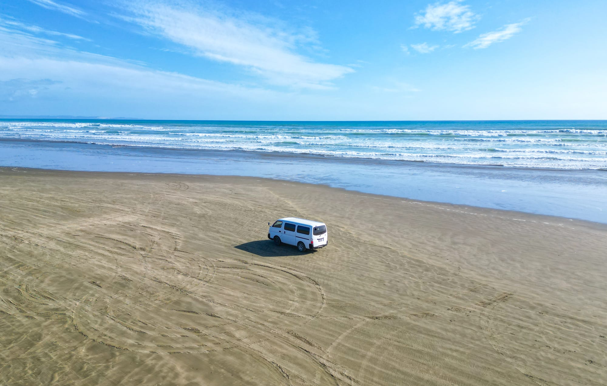 Vue aérienne d'un van blanc sur une plage en Nouvelle-Zélande